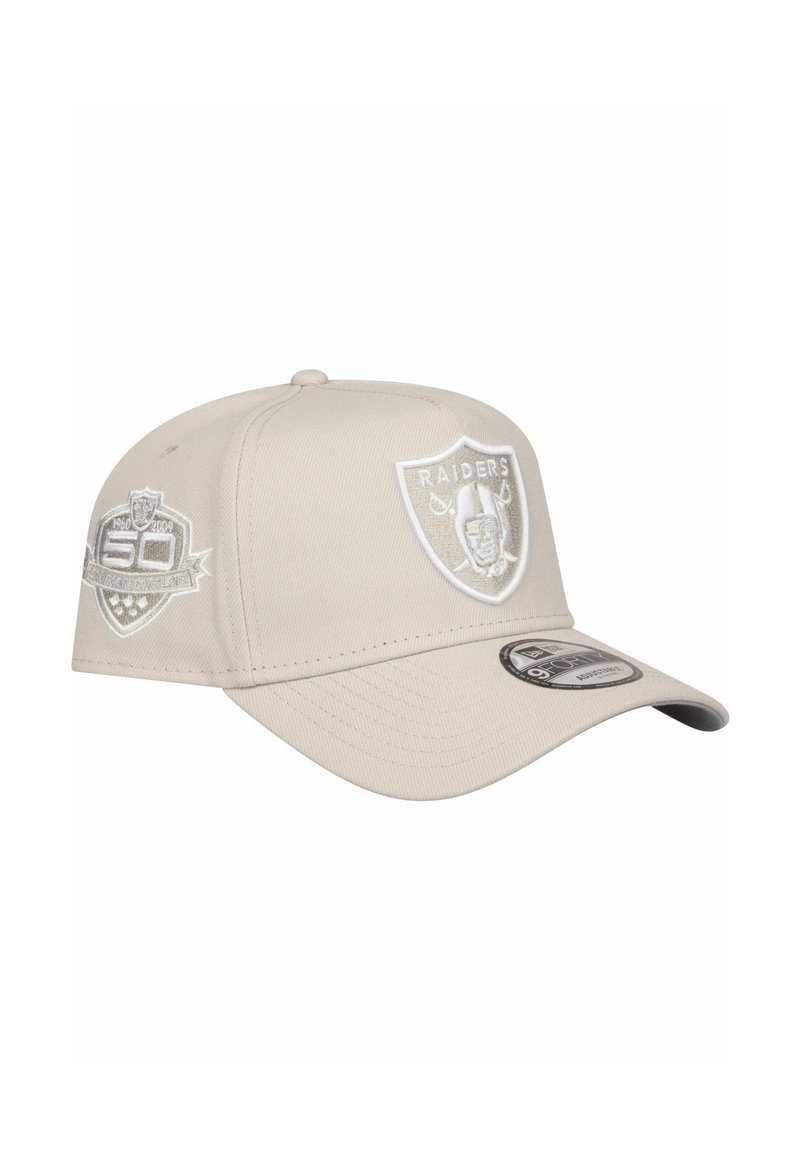 Beige Baseballcap mit gebogenem Schirm, ausgestattet mit weißen gestickten Logos, darunter das Raiders-Schild und ein Gedenkpatch.