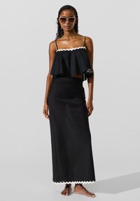 Fekete, két részes szett fodros, hullámos szegélyű crop topból és hozzáillő, hosszú szoknyából, mindkettő sima textúrájú anyagból.