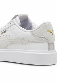 Baltie sporta apavi ar gludu ādu un zamšiem, ar perforācijām, teksturētu baltu zoli un zeltītu Puma logo uz papēža.
