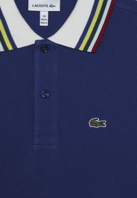 Marinblå polo shirt med strukturerad tyg, vit och flerfärgad randig krage, treknappslås och grön broderad krokodil-logotyp.