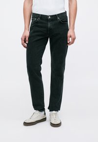 Sorte denimjeans med en klassisk pasform, der har lynlås, fem lommer og sølvfarvede knapdetaljer. Bæres med hvide sneakers.