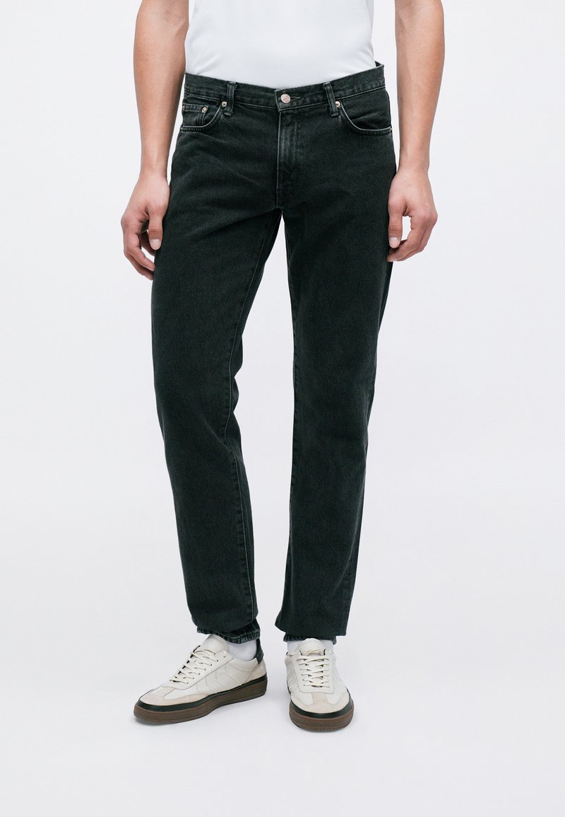 Sorte denimjeans med en klassisk pasform, der har lynlås, fem lommer og sølvfarvede knapdetaljer. Bæres med hvide sneakers.