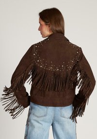 Brązowa skórzana kurtka z frędzlami na rękawach i plecach, ozdobiona srebrnymi ćwiekami, z klasycznym kołnierzem i zapięciem na zamek.