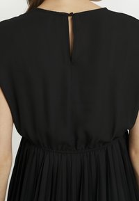 Musta mekko, jossa on sileä ja virtaava kangas. Ompelusmyötäinen hame joustovyöllä. Pyöreä kaula-aukko ja avaus niskaosassa.