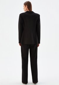 Svart kavaj med en strukturerad design, notch-krage och skräddarsydd passform, tillsammans med matchande raka byxor. Slät textur.