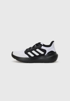 Zapatilla deportiva en blanco y negro con parte superior de malla, tres franjas blancas en el costado, suela negra y diseño de puntera redondeada.