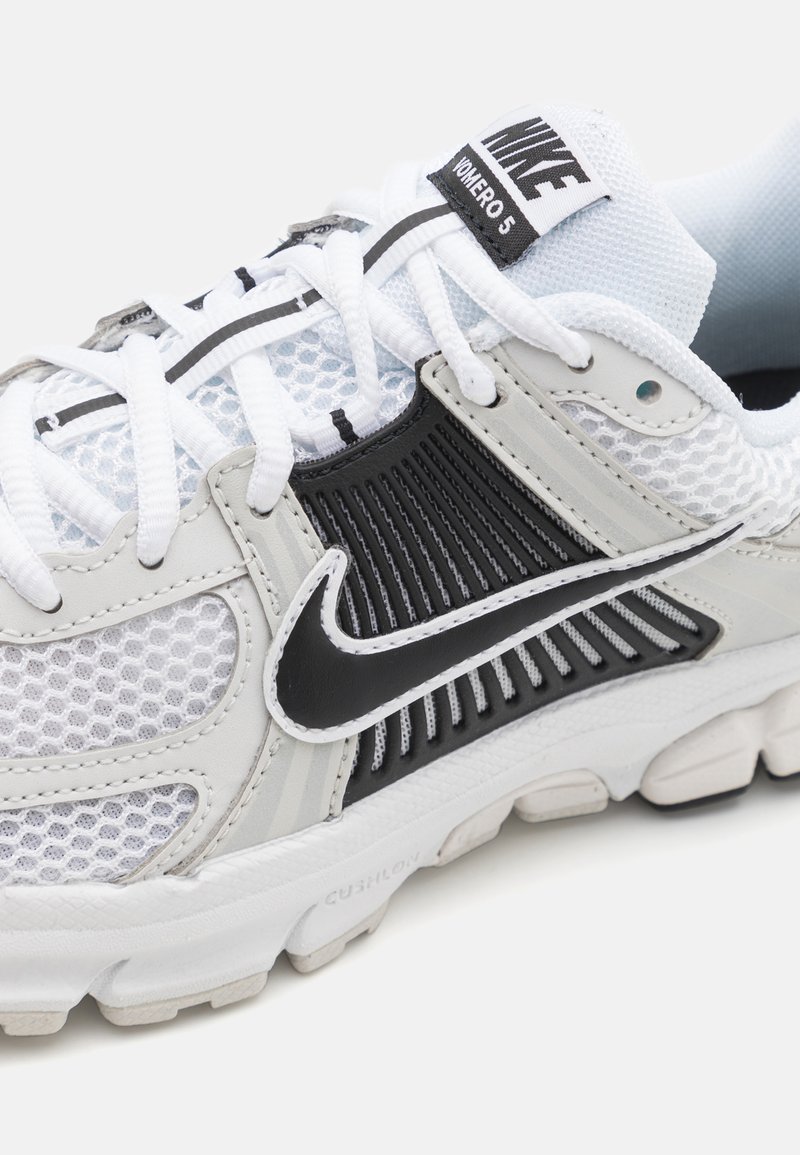 La sneaker Nike Air Zoom Vomero 5 présente une tige en mesh blanche avec des accents noirs, une semelle rembourrée et un design texturé avec des lacets.
