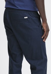 Tumši zili lina maisījuma bikses ar elastīgu jostasvietu, sānu kabatām un mazu birku aizmugurējā kabatā. Gluda tekstūra un brīvs griezums.