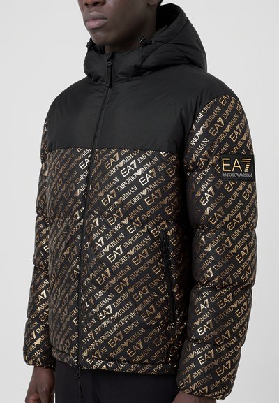 Модел носи черно яке с пухена подплата, златист надпис Emporio Armani, изчистен черен панел на гърдите и емблема на ръкава.