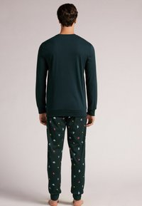 Top de manga larga verde oscuro con cuello redondo, combinado con pantalones verdes que presentan un patrón colorido de varias formas pequeñas. Textura de tela suave.