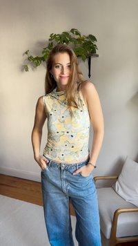 Top sem mangas com padrão floral em amarelo pastel, verde e azul; combinado com jeans de lavagem clara de cintura alta. Tecido com textura suave.