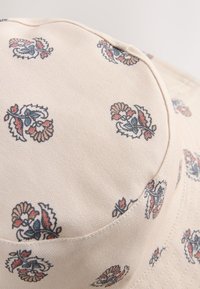 Beiger Fischerhut mit floralem Muster in Blau- und Rottönen. Hergestellt aus strukturiertem Stoff, mit abgesteppten Nähten und rundem Rand.