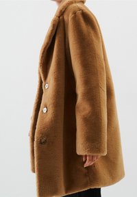 Abrigo marrón de gran tamaño fabricado con un material suave y texturizado, que presenta un cuello con muescas, dos botones y una silueta relajada.