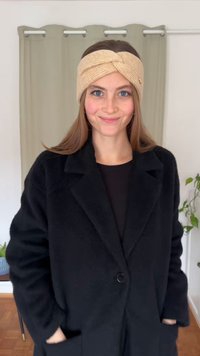 Adīta bēša galvas lente ar savītu dizainu un nelielu zelta akcentu; kombinēta ar melnu, teksturētu pārmērīga izmēra mēteļu.