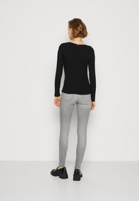 Schwarzes Langarmoberteil mit gerippter Textur, Rundhalsausschnitt und einem kleinen Detail auf der Rückseite. Kombiniert mit enganliegenden hellgrauen Jeans und schwarzen Schuhen.