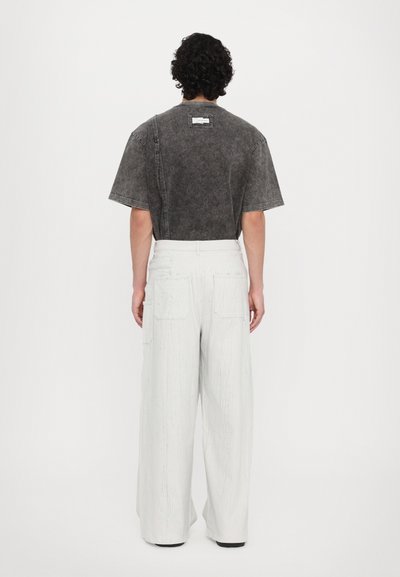 Camiseta gris corta con mangas cortas y un acabado texturizado, combinada con pantalones blancos de pierna ancha que cuentan con dos bolsillos traseros y un aspecto desgastado.