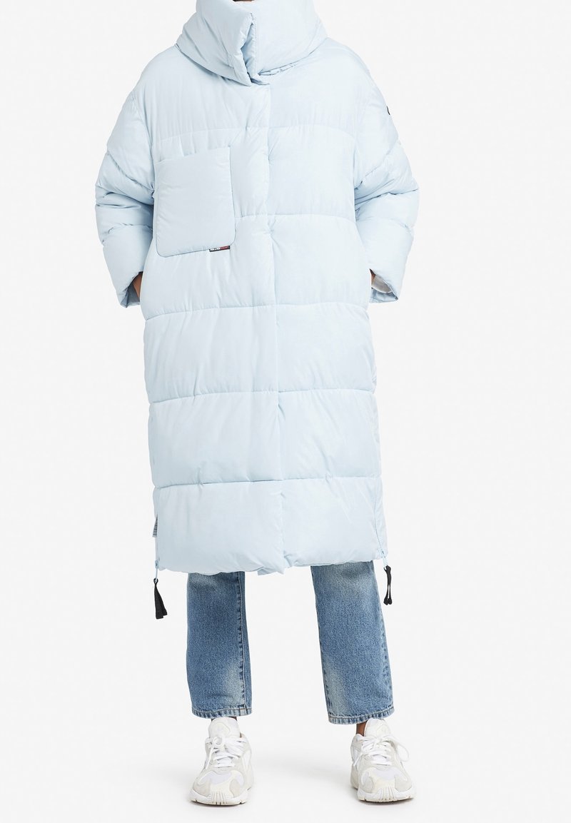 Ljusblå puffjacka med hög krage, framficka och stickade paneler. Buren över jeans och vita sneakers.