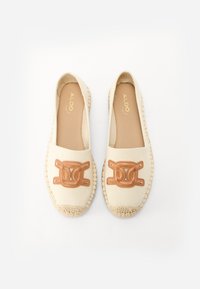 Beige espadrillet, joissa on kudottu juutikanta ja ruskea nahka-akentti, jossa on logo. Litteä kangaspinta, jossa on pyöristetyt varpaat.