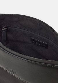 Bustina in pelle nera con chiusura a zip. Texture liscia, foderatura in tessuto e tasca interna. Piccolo logo impresso all'esterno.