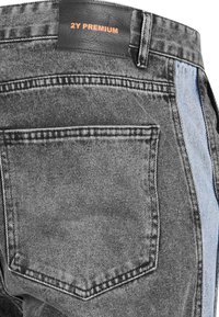 Pantalones de mezclilla negros con un panel en contraste azul claro, que incluye una etiqueta de cuero con "2Y PREMIUM" en naranja. Incluye un bolsillo trasero.
