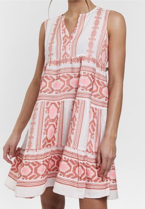 Robe blanche sans manches avec motifs floraux géométriques rose et orange, coupe ample avec jupe à volants, portée par une personne debout.