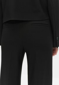 Czarne spodnie garniturowe o dopasowanym kroju, wykonane z gładkiego materiału, z dwiema tylnymi kieszeniami i czystymi liniami, uzupełnione pasującą marynarką.