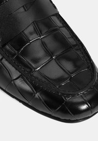 Zwarte leren loafers met een krokodillenpatroon, voorzien van een gladde textuur, een ronde neus en een vlakke zool. Aangevuld met een brede band.