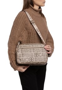 Borsa crossbody beige con loghi stampati, chiusura con zip e tracolla decorata. Realizzata in resistente materiale di tela con una finitura liscia.