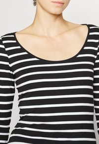 Frau trägt ein schwarz-weiß gestreiftes Langarmshirt mit breitem Rundhalsausschnitt.