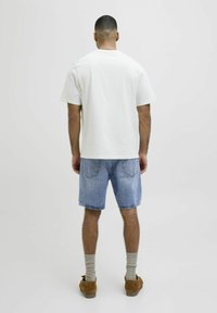 Camiseta blanca de manga corta, pantalones cortos de denim azules, calcetines beige y zapatos cómodos marrones. Ajuste casual, diseño simple y colores claros.