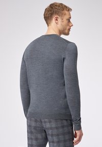 Grauer Pullover aus weichem Strickstoff, mit rundem Halsausschnitt und langen Ärmeln, kombiniert mit gemusterten grauen Karohosen.