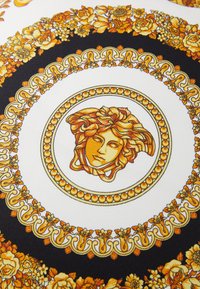 Tissu doré et noir avec des motifs floraux et un médaillon central affichant un visage stylisé, texturé avec des détails fins.