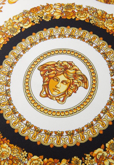 Gold and black patterned fabric featuring floral motifs and a central medallion with a stylized face, textured with fine details.
