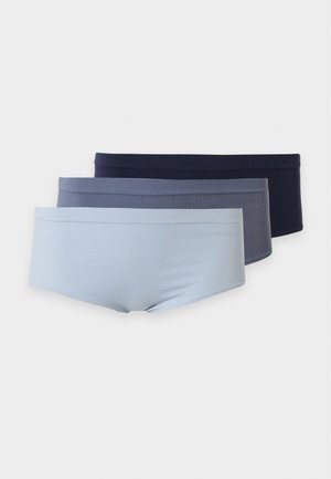 Frau mit langen dunklen Haaren, barfuß stehend in einem hellblauen Bralette und passender High-Waist-Unterwäsche vor einfachem weißem Hintergrund.
