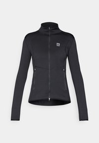 Giacca sportiva nera con colletto alto, zip frontale completa, due tasche con zip e dettagli di cucitura a contrasto. Tessuto liscio e elasticizzato.