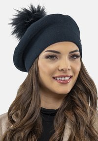 Beret negru din tricot cu un pompon pufoș pe vârf, având un design texturat și o potrivire strânsă, potrivit pentru vreme rece.