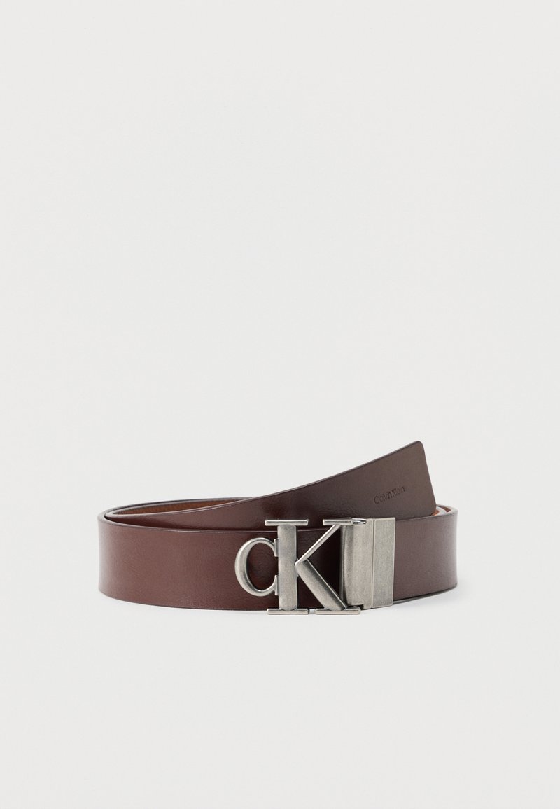 Ceinture en cuir brun enroulée avec une boucle métallique "CK" logo, design minimaliste sur fond blanc uni.