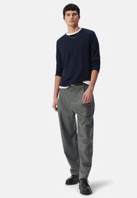 Granatowy sweter z długim rękawem nałożony na biały t-shirt z okrągłym dekoltem, połączony z luźnymi szarymi spodniami i czarnymi sznurowanymi butami. Prosty krój, miękka tekstura.