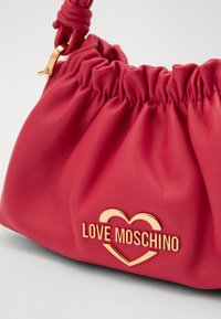 Red leather handbag with gathered design, gold hardware, featuring "LOVE MOSCHINO" logo in a heart shape at the front. Textured finish.