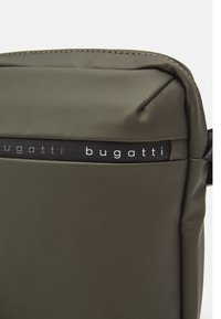 Maslinasto zelena Bugatti torba glatke teksture, s crnom logotip trakom i minimalističkim dizajnom. Kompaktan pravokutni oblik s suptilnim šavovima.