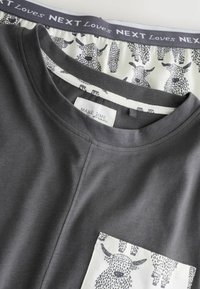 Grijs katoenen t-shirt met een voorzak met een zwart-wit dierenprint. De halslijn is rond en de stof lijkt zacht.