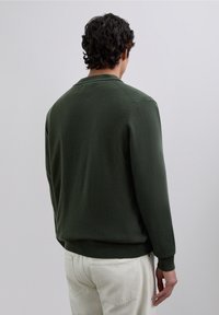Suéter de punto verde con cuello redondo, mangas largas y puños y dobladillo acanalados. Textura suave y un diseño sencillo.