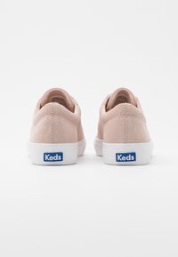 Růžové semišové tenisky s bílými gumovými podrážkami a modrým logem "Keds" na patě, s kulatým tvarem a měkkou texturou.