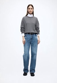 Γκρι φούτερ και μπλε τζιν με φαρδιά μπατζάκια, συνδυασμένα με λευκό ζιβάγκο. Η εμφάνιση ολοκληρώνεται με μαύρη ζώνη και απλά μαύρα παπούτσια.