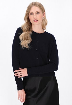 Cardigan lavorato a maglia blu navy con maniche lunghe, scollatura rotonda, cinque bottoni, polsini a costine e una piccola tasca sul lato sinistro del petto.