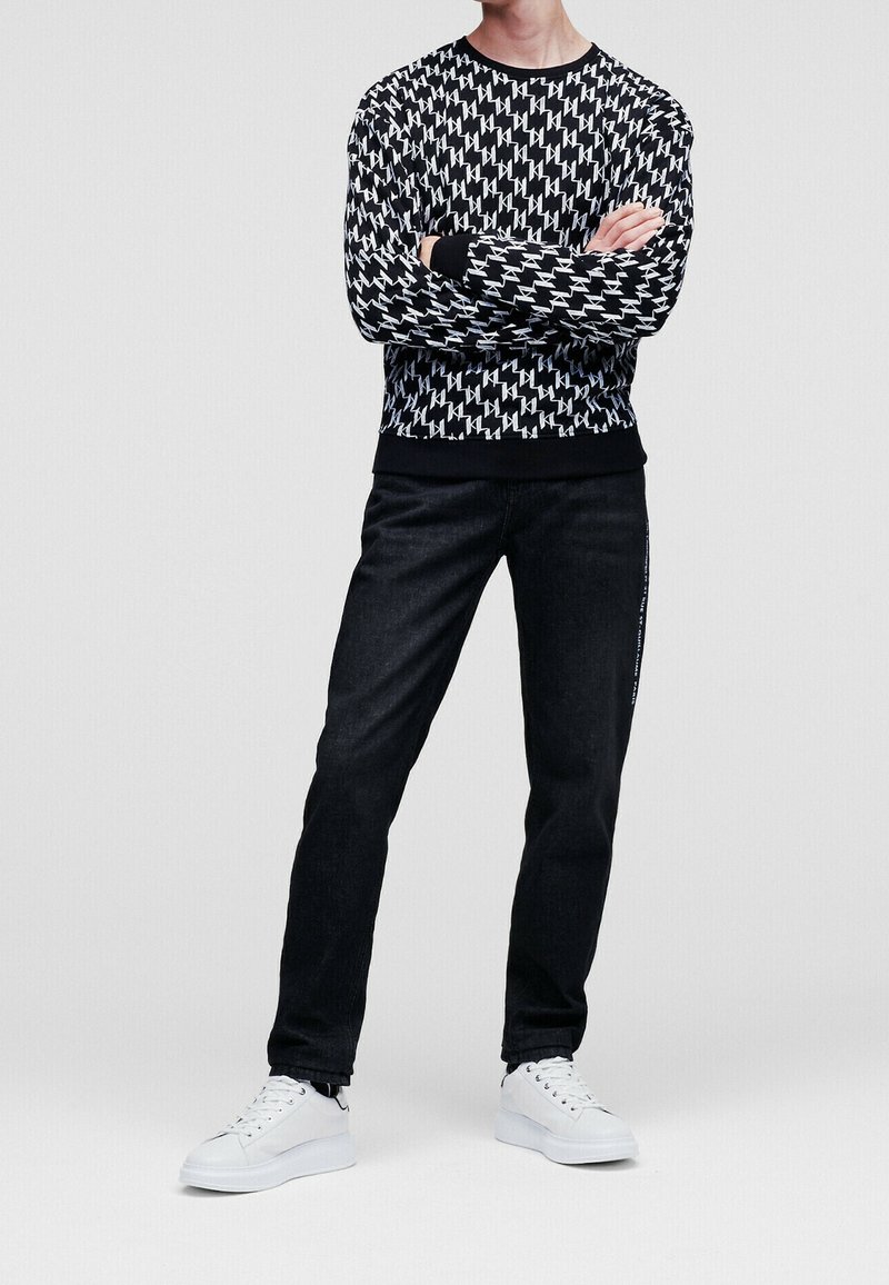 Pull à motif noir et blanc avec un col rond, assorti à un jean foncé et des baskets blanches. La tenue met en valeur des textures et des couleurs contrastées.