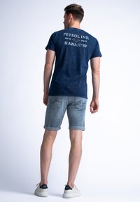 Donkerblauwe t-shirt met witte bedrukte tekst op de achterkant, gecombineerd met lichtgrijze opgerolde shorts en witte sneakers met donkere accenten.