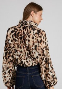 Blusa con estampado de leopardo, con escote fruncido, textura plisada y mangas largas. La paleta de colores incluye tonos beige, marrón y negro.