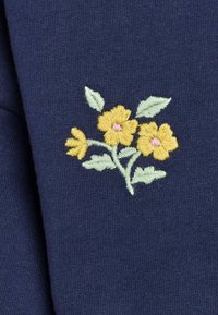 Ricamo di fiori gialli con foglie verdi su un tessuto blu scuro.