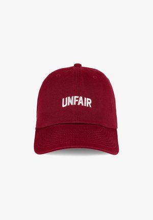 Red cotton cap with a curved visor and adjustable strap. Features "UNFAIR" embroidered in white across the front. Textured fabric.